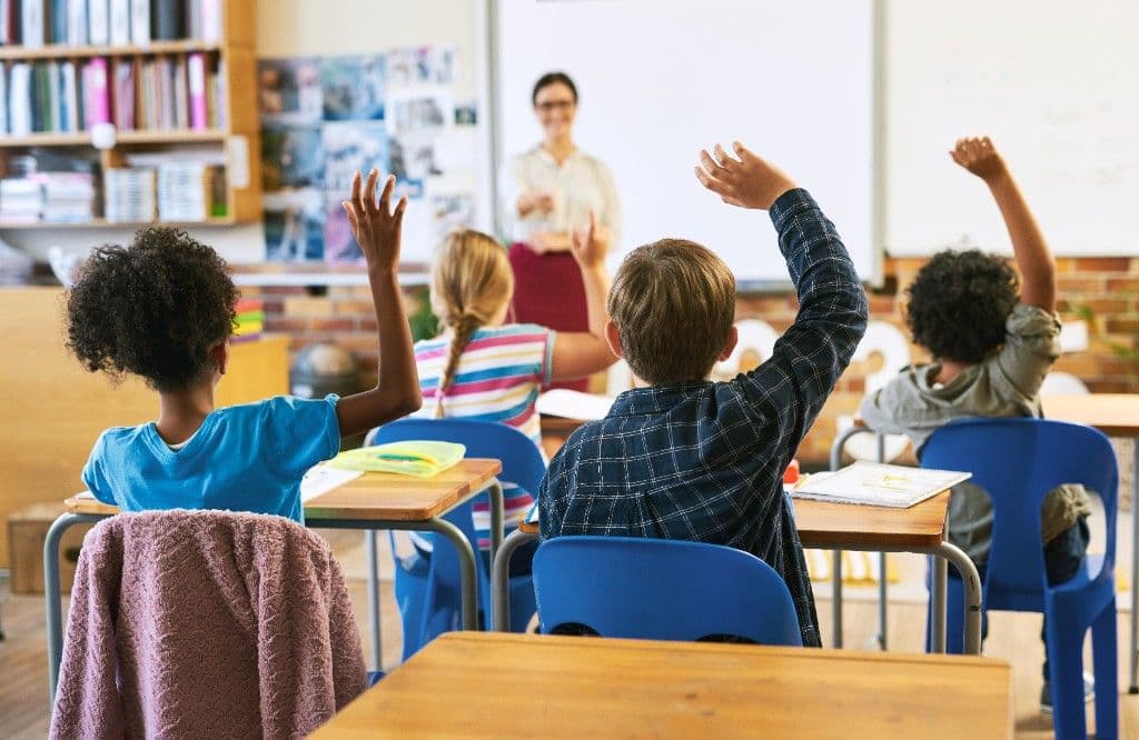 Élèves levant la main en classe devant leur enseignante